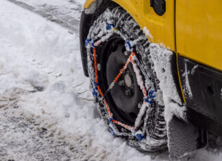 Zimná dilema: Kedy sú snehové reťaze povinné? Osobné auto so snehovými reťazami nasadenými na pneumatikách počas jazdy po zasneženej horskej ceste.