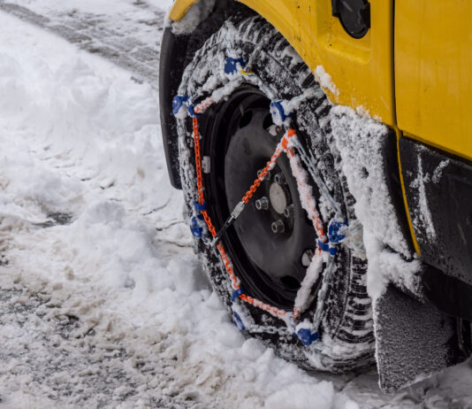 Zimná dilema: Kedy sú snehové reťaze povinné? Osobné auto so snehovými reťazami nasadenými na pneumatikách počas jazdy po zasneženej horskej ceste.